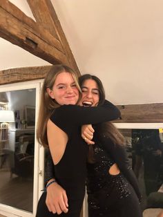 two young women hugging each other in front of a window with wooden beams on the wall