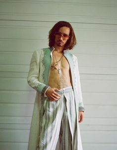 a man with long hair and no shirt standing in front of a wall wearing sunglasses