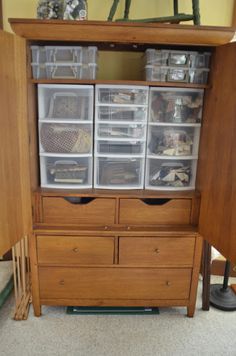 an open cabinet with plastic containers on top and drawers below it, in a living room