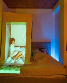 a woman sitting on top of a bed in a room with yellow curtains over it