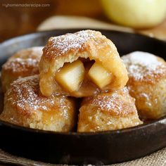 some sugary pastries are in a black bowl on a table next to an apple