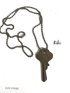 an old key is attached to a chain on a white background with the word kiki written below it