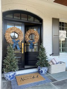 two wreaths on the front door of a house with blue and white pots holding christmas trees