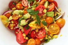 a salad with tomatoes, corn and avocado is shown in a white bowl