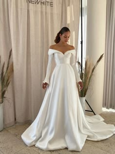 a woman in a white wedding dress standing next to a window with her hands on her hips