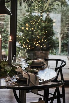 a table set for two with candles and christmas tree in the backgroung