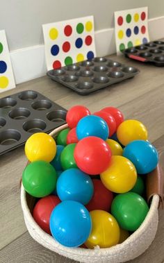 a bowl filled with lots of colorful plastic balls on top of a wooden table next to muffin tins