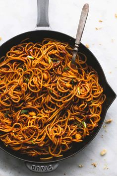 a skillet filled with noodles on top of a white counter next to a spoon