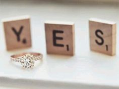 two engagement rings sitting on top of wooden blocks with the word yes spelled by them