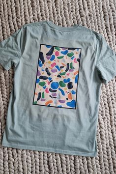 a t - shirt with an abstract design on the front and back, sitting on a bed