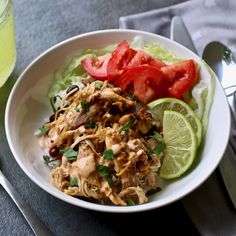 a white bowl filled with meat, rice and vegetables next to sliced lime wedges