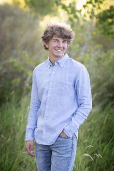 a young man standing in tall grass with his hands in his pockets and smiling at the camera