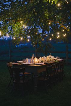 an outdoor dinner table set up under a large tree with lights strung from the branches