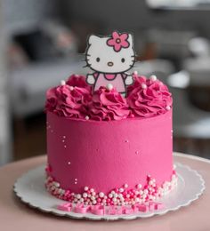 a hello kitty cake with pink frosting and sprinkles on top, sitting on a plate