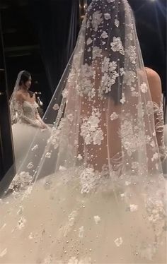 a woman in a wedding dress looking at herself in the mirror with flowers on her veil