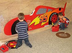 two young boys playing in front of a red race car on the floor with other children