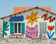 a house painted with flowers and cats on the side, in front of a desert landscape