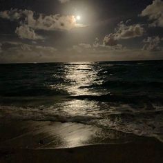 the moon is setting over the ocean on a cloudy day with waves lapping in front of it