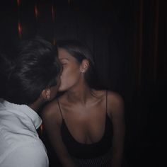 a man kissing a woman in the dark with her face close to her chest as she stands next to him