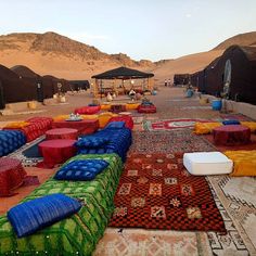 an outdoor area with many colorful pillows and rugs on the ground in front of mountains