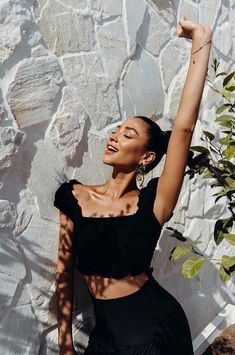 a woman in a black crop top and skirt posing for a photo with her arms up