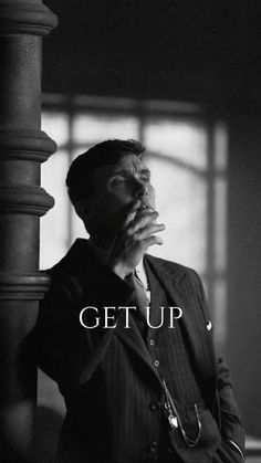 a man in a suit and tie leaning against a pillar with the words get up above him