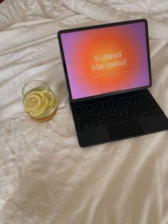 an open laptop computer sitting on top of a bed next to a glass of beer