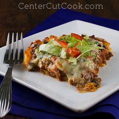 a square white plate topped with lasagna covered in cheese and lettuce