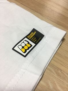 a white shirt with a black and yellow label on it sitting on a wooden table