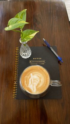 a cup of coffee sitting on top of a wooden table next to a notepad