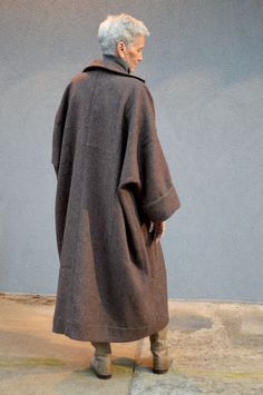 an older woman is standing in front of a blue wall wearing a coat and boots