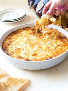 a person dipping some tortilla chips into a casserole dish with cheese