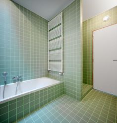 a bathroom with green tiles and a white bathtub next to a wall mounted radiator