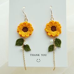 a pair of sunflower earrings with chains hanging from it's ear ends, on top of a card that says thank you