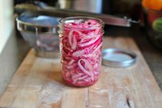 a jar filled with red onions sitting on top of a wooden cutting board