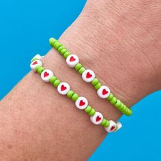 two green and white bracelets with red hearts on each one hand, set against a blue background