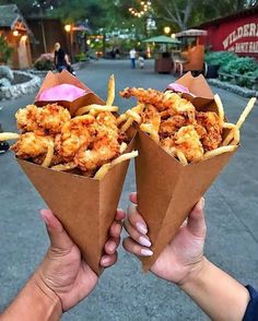 two people holding up cones filled with fried food on top of each other in front of a restaurant