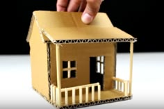 a hand is holding up a small house made out of construction paper and cardboard boxes