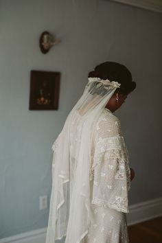 a woman in a wedding dress and veil looking at the wall with a clock on it