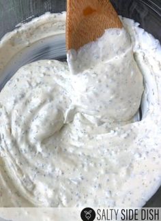 a wooden spoon in a bowl filled with white ranch dips and sauce on the side