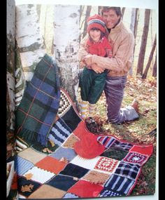 two people standing next to each other in front of a tree with blankets on it