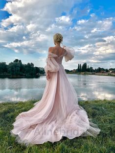 a woman in a pink dress is standing on the grass next to a body of water