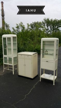 two white cabinets sitting in the middle of a parking lot next to bushes and trees