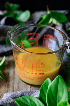 a measuring cup filled with liquid on top of a wooden table next to green leaves