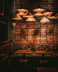 an empty restaurant with wooden tables and stools in front of a brick wall that has hanging lights above it