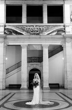 a bride standing in the middle of a large hall with columns and arches on either side