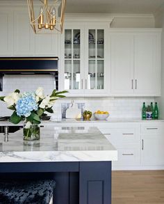 a white kitchen with marble counter tops and blue stools in front of the island