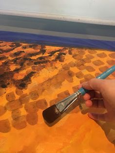 a person holding a paintbrush in front of an orange and brown painting with squares on it