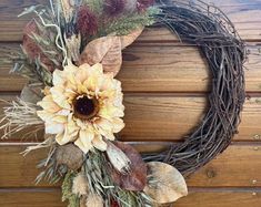 a wreath with dried leaves and sunflowers on it sitting against a wooden wall