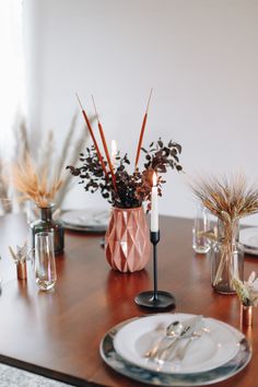 a wooden table topped with plates and vases filled with flowers